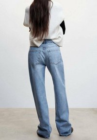 Jeans de tiro alto en azul claro con un corte recto, que presentan bolsillos traseros y una textura ligeramente desgastada. Se combinan con un suéter en color crema y negro.