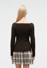 Ruda, briaunuota ilgomis rankovėmis palaidinė su plačiu iškirpimu, dėvima viršutiniu sluoksniu ant languotos sijono, kuriame dominuoja rudos ir kūno spalvos atspalviai. Lygios audinio tekstūros.