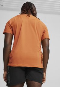 Kortærmet, orange atletisk skjorte med tekstureret stof, der har et sort trykt logo langs siden og et lige rygdesign.