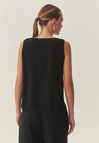Črna brezrokavnik z ohlapnim krojem, ki ima gladko teksturo in raven rob, ter razkriva gola ramena in hrbet.