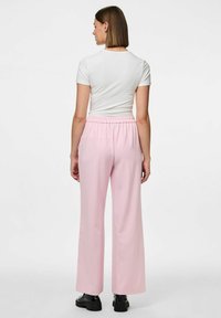 Pantalons larges rose clair avec une taille élastique, associés à un haut blanc ajusté ; tissu lisse, design minimal et sans motifs visibles.