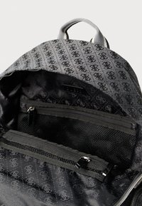 Nahrbtnik iz sive tkanine z enakomernim vzorcem črnih logotipov. Notranji žepi: en mrežast, en z zadrgo. Gladek tekstura, trdna izdelava.