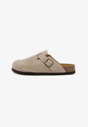 Sabot en suède beige avec un bout arrondi, un dos ouvert et un accent de boucle en métal. Semelle texturée marron avec des grips pour une meilleure adhérence.