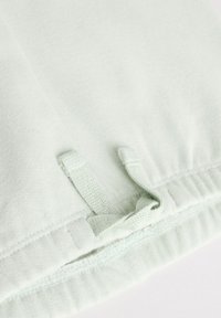Tissu vert clair à la texture douce avec une ceinture élastique et un cordon de serrage doté de deux boucles en tissu pour l'ajustement.