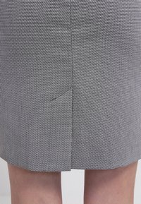 Jupe mi-longue en motif pied-de-poule noir et blanc, avec une fente arrière pour le mouvement, texture lisse et coupe ajustée.