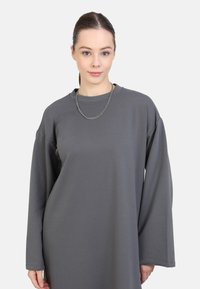 Indumento grigio oversize a maniche lunghe con scollatura rotonda, realizzato in un tessuto morbido, caratterizzato da spalle cadenti e una consistenza liscia.