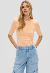 Pfirsichfarbendes, tailliertes T-Shirt mit kurzen Ärmeln, Rundhalskragen und gerafften Seitendetails, kombiniert mit hellblauen, weit geschnittenen Denim-Cargo-Hosen.