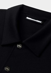 Polo nero realizzato in tessuto texturizzato, con colletto classico e bottoni esagonali argentati con dettagli incisi.