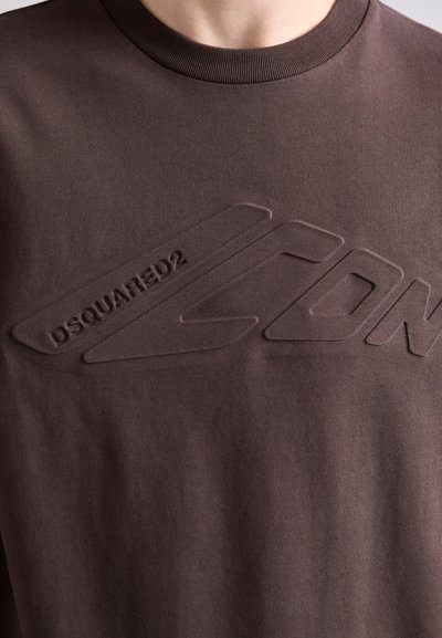 Camiseta marrón con un diseño de logo en relieve y tono que dice "DSQUARED2 ICON". Cuello redondo con un acabado suave. Tejido de algodón suave.