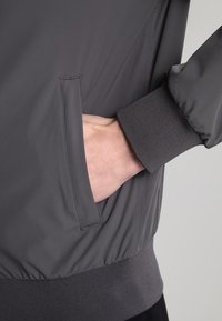 Gray bomber jacket with a smooth finish, ribbed cuffs, and side pockets. Features a relaxed fit and gathered waistband for comfort.