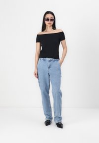 Fekete, vállnélküli blúz, világoskék, laza szabású farmernadrág és fekete, hegyes orrú balerina cipő. A modellen sötét napszemüveg van; minimalista háttér.