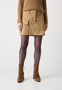 Kaki skjørt med en strukturert design, med to frontlommer. Matchet med brune semskede ankelstøvler og svarte semi-opaque strømpebukser.