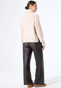 Cremfarbener Rollkragenpullover mit geripptem Saum, kombiniert mit weit geschnittenen Hosen aus dunkelbraunem Leder und hellbraunen Slippern.