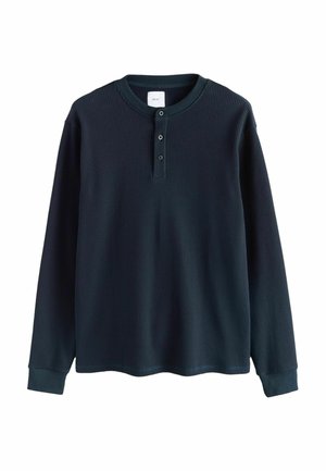 Chemise Henley à manches longues en tricot gaufré bleu foncé avec trois boutons et des poignets côtelés, posée à plat sur un fond blanc.