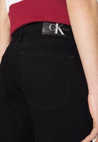 Jean de mezclilla negra con una textura suave, que presenta bolsillos traseros y una etiqueta del logo de Calvin Klein Jeans en la cinturilla.