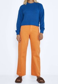 Blå ribbad stickad tröja ihop med orange vida byxor och bruna texturerade sandaler med öppet tåparti, med fokus på livliga färger och avslappnad passform.