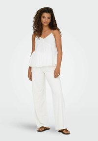 Witte mouwloze top met kantaccenten en een vloeiende silhouet, gecombineerd met witte wijde broek en bruine sandalen. Gladde, lichtgewicht stof.
