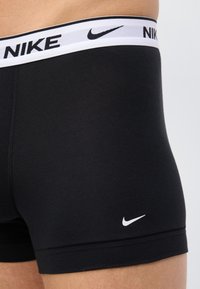 Κοντινό πλάνο ατόμου που φοράει μαύρα εσώρουχα boxer της Nike με λευκή μέση που φέρει το λογότυπο της Nike και το σήμα swoosh στο μηρό.