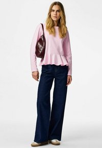 Lys rosa langermet peplum-topp kombinert med vide mørkeblå jeans, supplert med en burgunder skulderveske og beige sko.