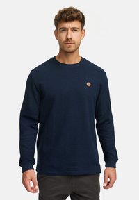 Mørkeblå langærmet sweatshirt lavet af tekstureret stof med ribbet halsudskæring og et lille rundt logo på brystet.