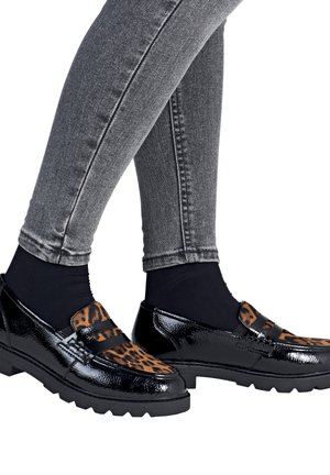 Jambes en jean gris, chaussettes noires et mocassins en cuir verni noir avec des détails en imprimé léopard marron sur le dessus.