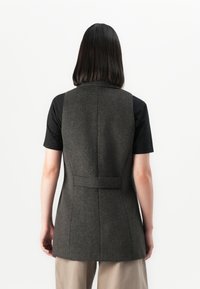 Vest din lână gri cu un design ajustat, cusături pe spate și detalii cu curea. Pur și simplu peste o cămașă neagră cu mânecă scurtă, împreună cu pantaloni de culoare neutră.