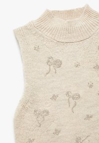Maglioncino beige senza maniche con colletto alto, caratterizzato da fiocchi e stelle ricamati in argento su tutta la superficie.