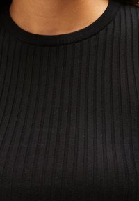 Černá žebrovaná tričkovina s texturovaným vzorem svislých pruhů a kulatým výstřihem. Měkký, přiléhavý materiál.