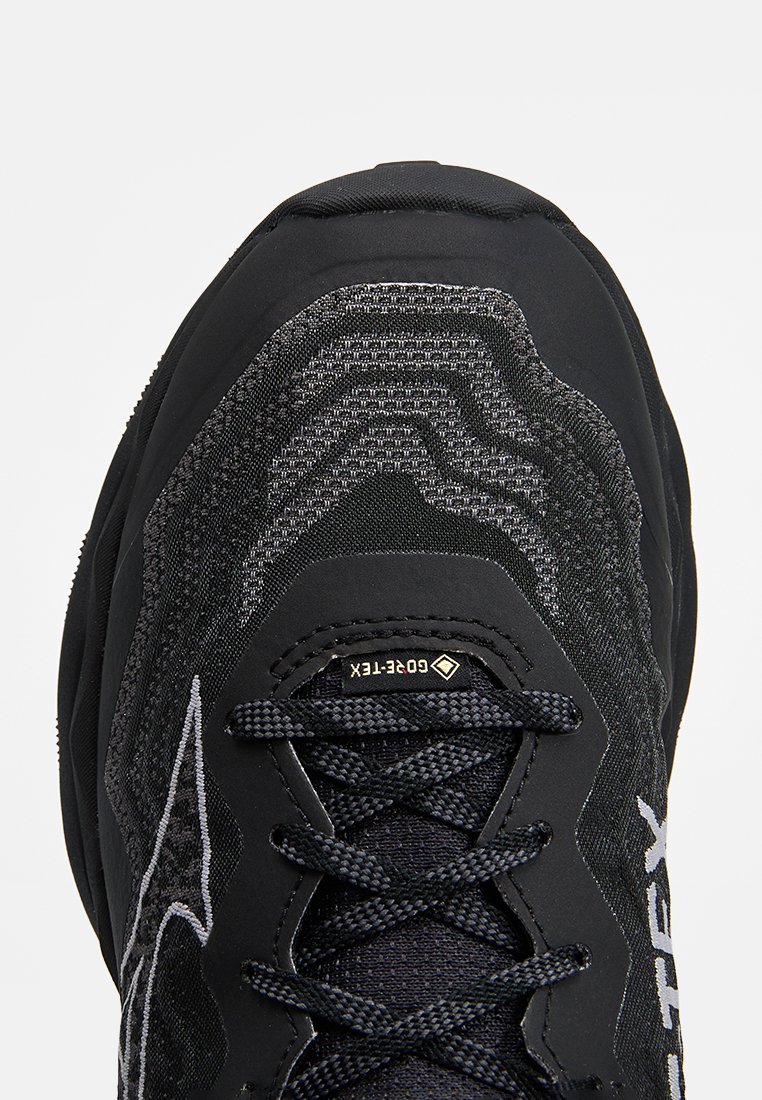 Czarne buty sportowe z teksturowanym cholewką w geometryczne wzory, wzmocnionym noskiem i podeszwą o dobrej przyczepności. Sznurowadła są czarne z minimalnym logotypem.