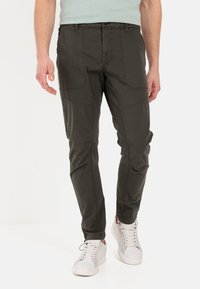 Dunkelgrüne, leichte Chinos mit schmaler Passform, ausgestattet mit Vordertaschen und sichtbaren Nähdetails, kombiniert mit weißen Sneakers.