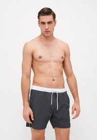 Bañador gris hecho de tejido ligero con una cinturilla elástica blanca, cordón y bolsillos laterales; diseño simple sin patrones.