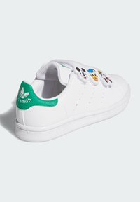 Sneaker bianchi in pelle con accenti verdi, dotate di toppe dei personaggi Disney sulla linguetta e suola in gomma texturizzata.