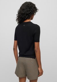 Maglione lavorato a maglia nero a maniche corte con scollatura rotonda, abbinato a pantaloni corti a quadri marroni e neri, dotati di un orlo leggero e lavorazione a maglia testurizzata.