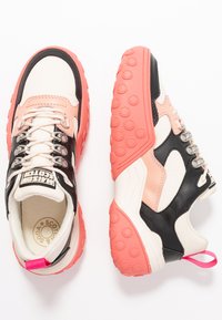 Die Turnschuhe bestehen aus einer Mischung aus schwarzen, rosa und cremefarbenen Materialien, mit einer strukturierten Gummisohle, Metallösen und einer Zuglasche für ein einfaches Anziehen.