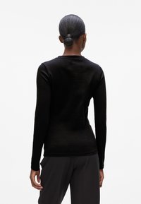 Maglia nera a maniche lunghe con una consistenza liscia, scollatura rotonda e design aderente, vista da dietro, abbinata a pantaloni scuri.