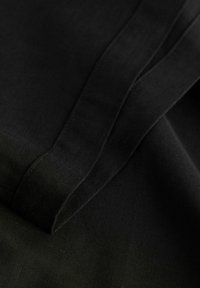 Tissu noir à texture lisse, présentant de légers plis et coutures. Le matériau semble doux et léger.