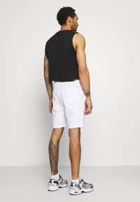 Top negro sin mangas combinado con pantalones cortos blancos, que cuentan con un bolsillo trasero. El modelo lleva zapatillas grises y blancas con acentos negros.