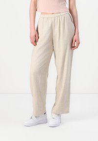 Pantaloni largi bej cu o finisare texturată, cu un brâu elastic și buzunare laterale, asortați cu adidași albi.