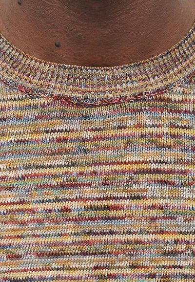 Κοντινό πλάνο ενός πολύχρωμου πλεκτού γιακά πουλόβερ σε σκούρο δέρμα με μια μικρή σκοτεινή ελιά πάνω από το λαιμό.