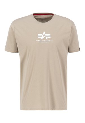 Bež pamukasta majica s okruglim izrezom, sa bijelim printanim logotipom "ALPHA INDUSTRIES" na prsima i crvenim detaljima unutar ovratnika.