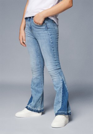 Jean évasé bleu clair avec un ourlet brut, présentant un design bicolore. Le tissu semble être en denim avec un léger effet délavé et une coupe classique.