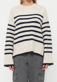 Pull rayé avec des rayures horizontales crème et bleu marine, texture côtelée, encolure ronde et épaules tombantes ; coupe décontractée avec manches larges.