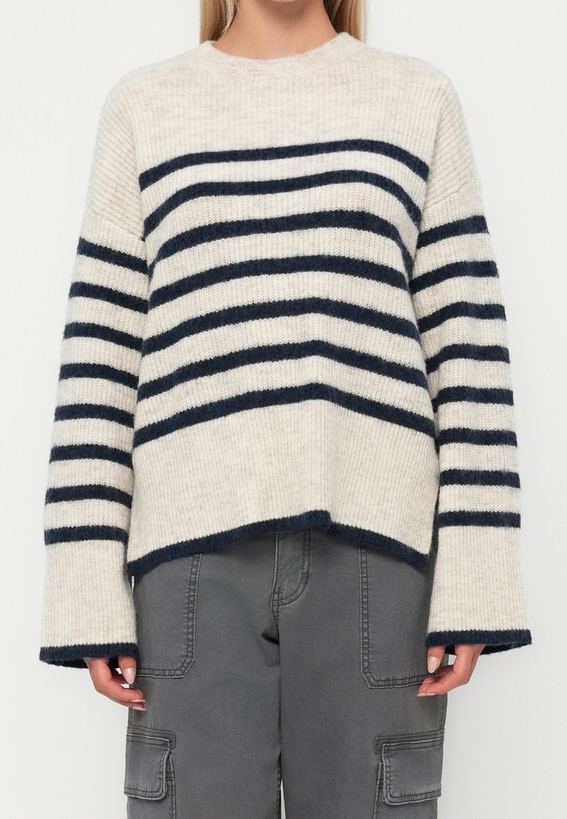 Pull rayé avec des rayures horizontales crème et bleu marine, texture côtelée, encolure ronde et épaules tombantes ; coupe décontractée avec manches larges.