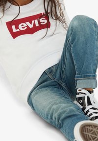 Vit sweatshirt med en röd Levi's-logotyp, i kombination med blå denimjeans. Svartvita tygskor. Avslappnad passform, avslappnad stil.
