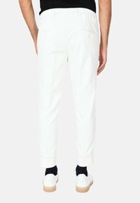 Pantaloni in corduroy bianchi con taglio slim, fascetta elastica in vita e orli arrotolati, abbinati a sneaker bianche e calzini neri.