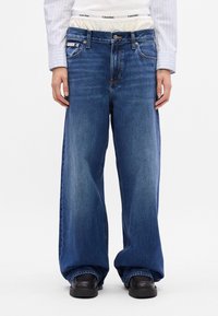 Niebieskie dżinsy wide-leg marki Calvin Klein o luźnym kroju, z pięcioma kieszeniami, zapięciem na guzik i teksturowanym pasem.