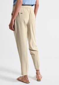 Beige avsmalnande byxor i ett strukturerat tyg, med elastisk midja och en enda bakficka. Matchas med ljusbruna snörsandaler.
