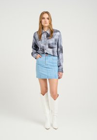 Pilkos ir juodos abstrakčios patterned marškiniai, derinami su šviesiai mėlyna džinsiniu mini sijonu ir baltomis aukštakulnėmis batais iki kelių.