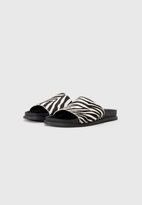 Svartvita sandaler med zebramönster, slät yta, öppen tådesign och platt gummisula för komfort.