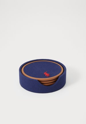 Sous-verres ronds en tissu bleu marine avec un motif chevron, entourés d'un bord en cuir beige et arborant un logo rouge brodé au centre.